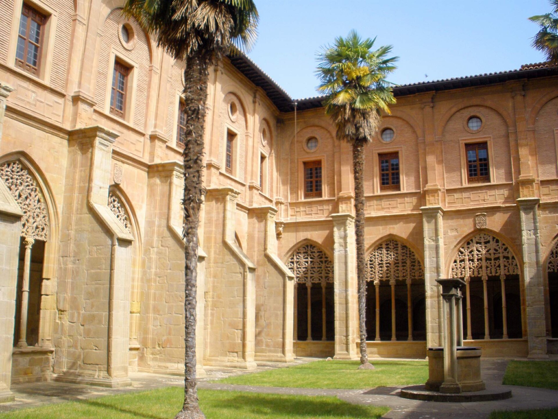 Claustro de los Caballeros del Monasterio de Santa María la Real de Nájera, con arcos de tracería gótica, palmeras y un pozo en el patio