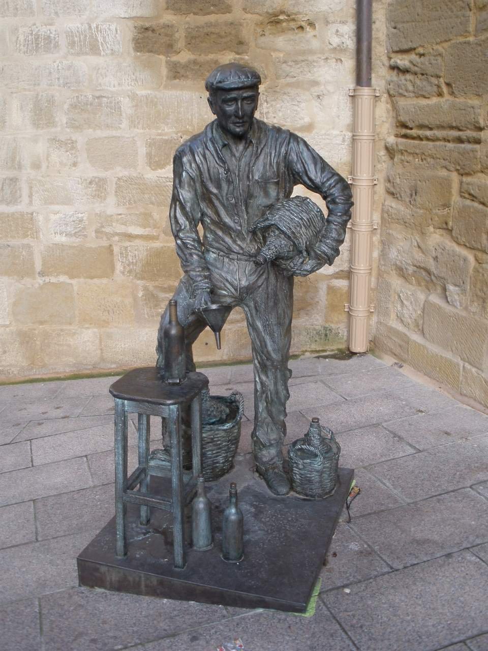 Escultura de bronce a tamaño natural de un artesano del vino junto a una fachada de piedra en el casco antiguo de Haro