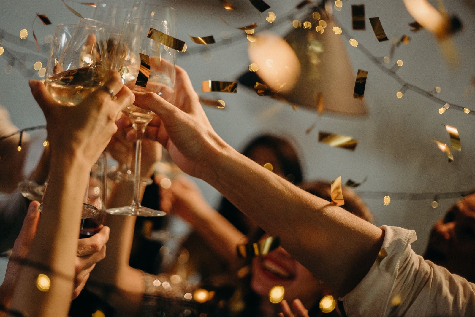 Grupo de amigos brindando con copas de espumoso entre confeti dorado en una celebración de Nochevieja